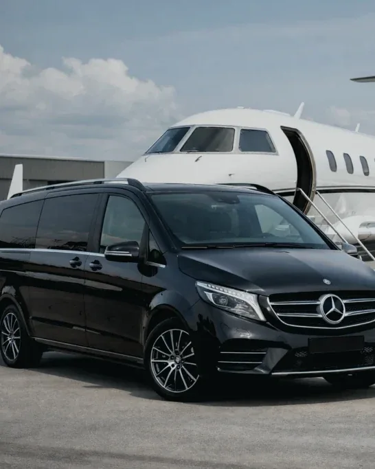 Monovolumen negro con chófer esperando junto a un avión privado en pista