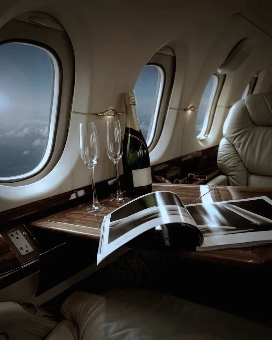 Cabina de un avión privado con copas, botella y una revista sobre la mesa